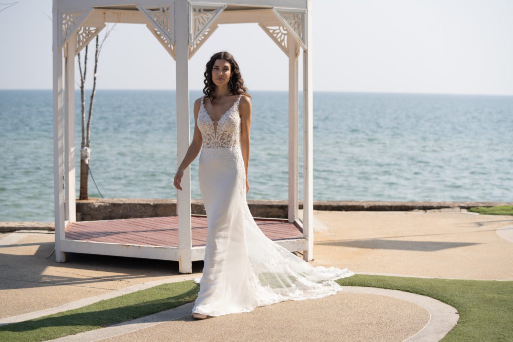 Een mooie vrouw dat in haar witte bruidsjurk staat bij een altaar en een open zee op de achtergrond.