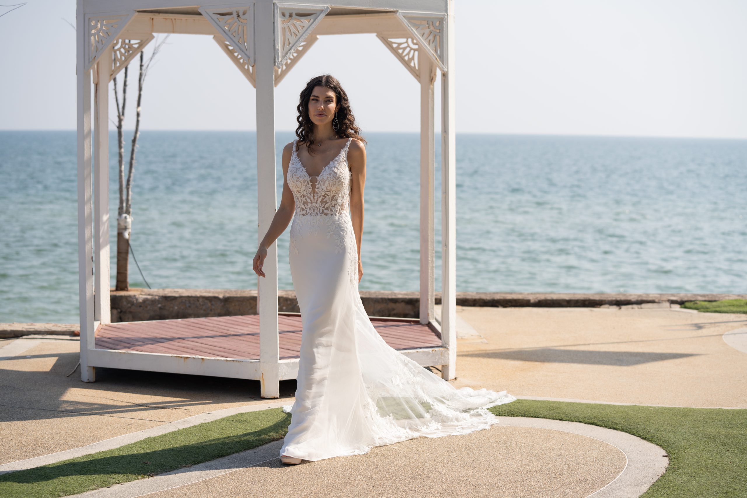 Een mooie vrouw dat in haar witte bruidsjurk staat bij een altaar en een open zee op de achtergrond.